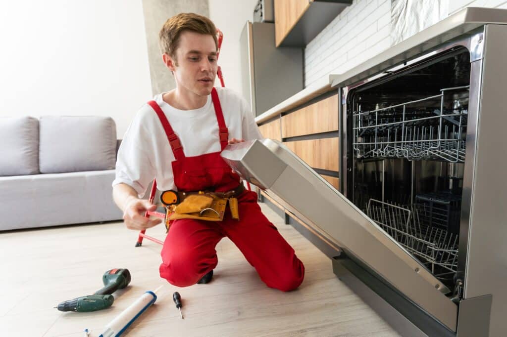 Repair of dishwashers. Repairman repairing dishwasher in kitchen